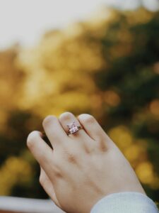 Close-up of an elegant engagement ring on a woman's hand with a natural outdoor setting in the background.